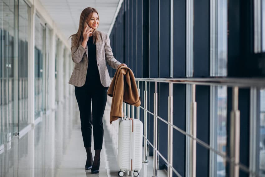 Business woman in terminal with travel bag talking on phone
